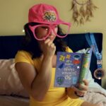 Woman sitting in a thinking pose with oversized goofy glasses reading an upside down book