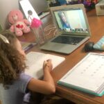 Child sitting at desk taking a class on a laptop.