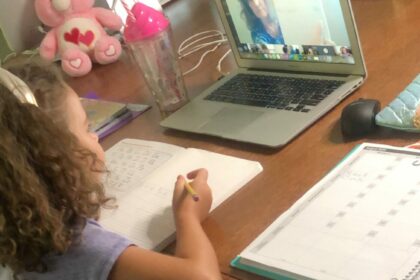 Child sitting at desk taking a class on a laptop.