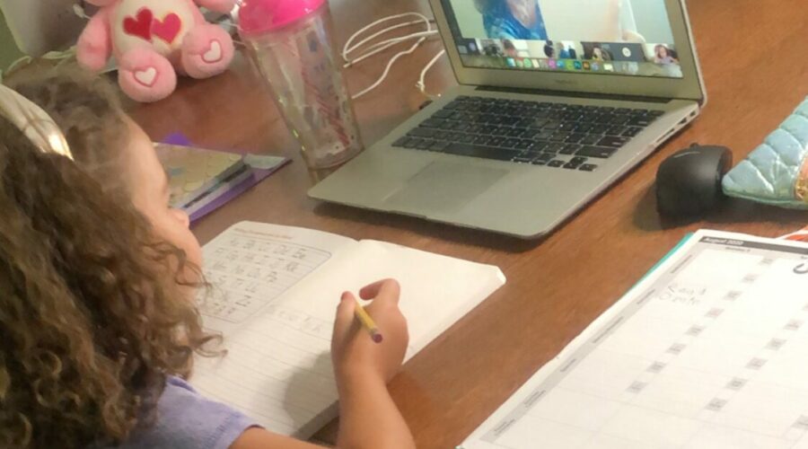 Child sitting at desk taking a class on a laptop.