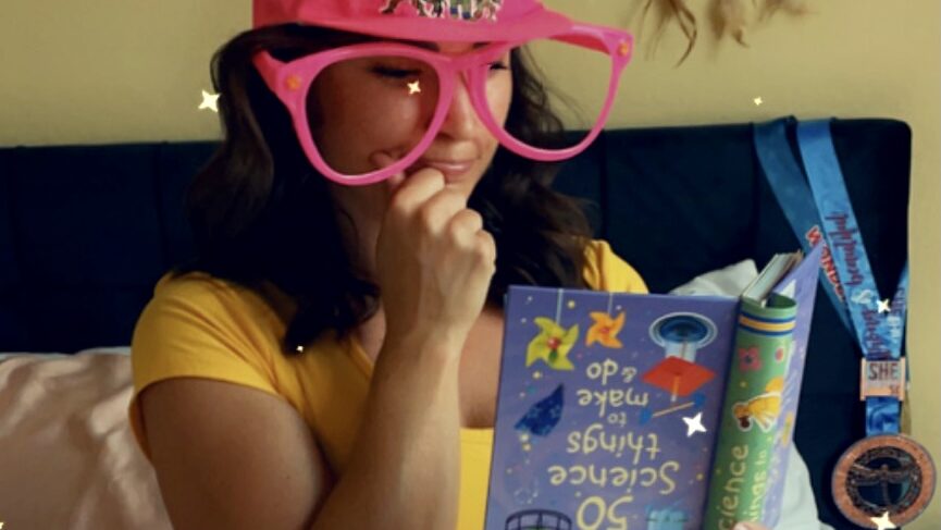 Woman sitting in a thinking pose with oversized goofy glasses reading an upside down book