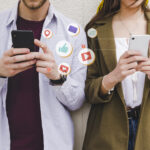 Two people holding cell phones with social media icons indicating social media use